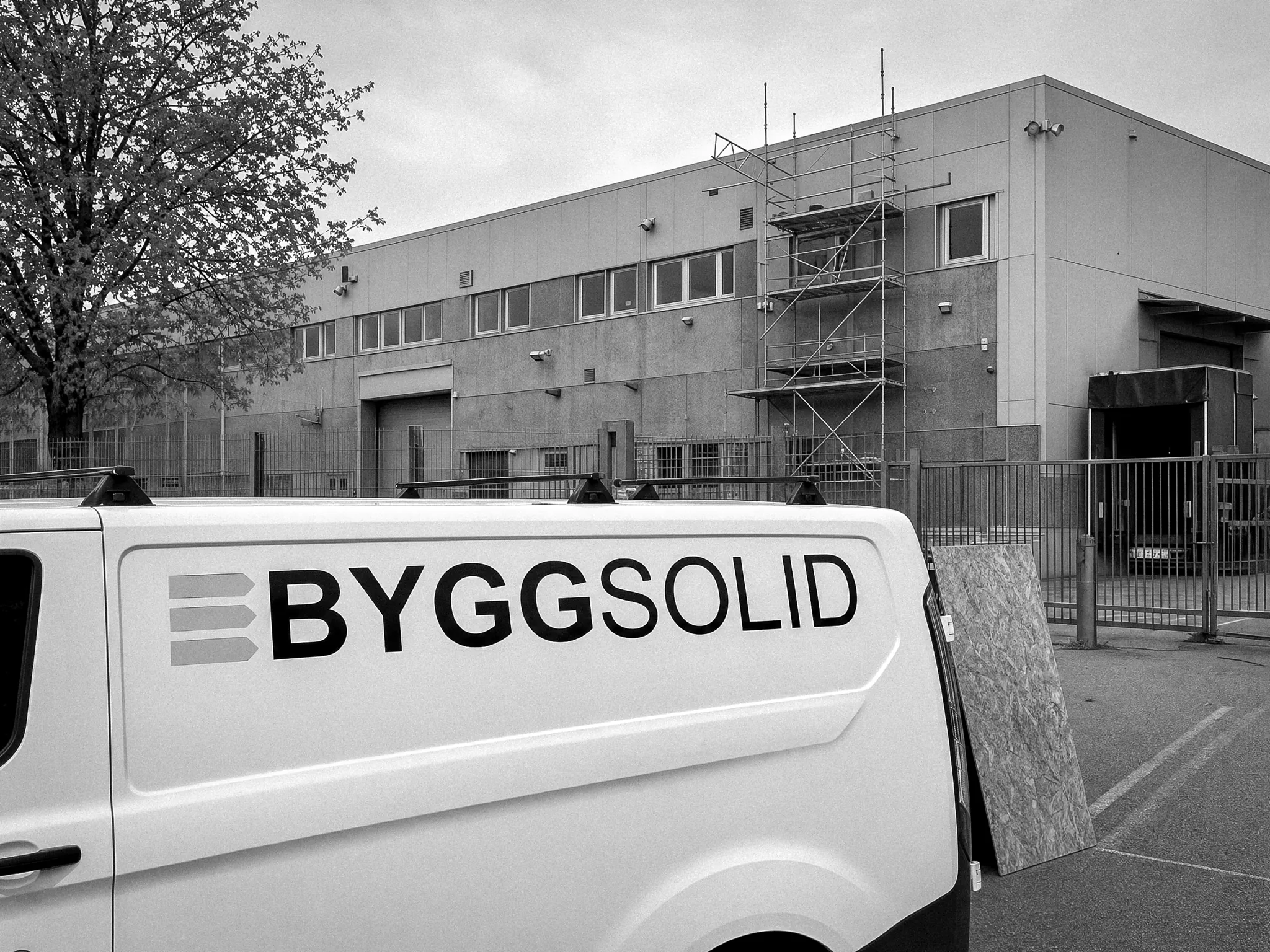 Byggsolids servicebil utanför en inhägnad anläggning med ställning på fasaden